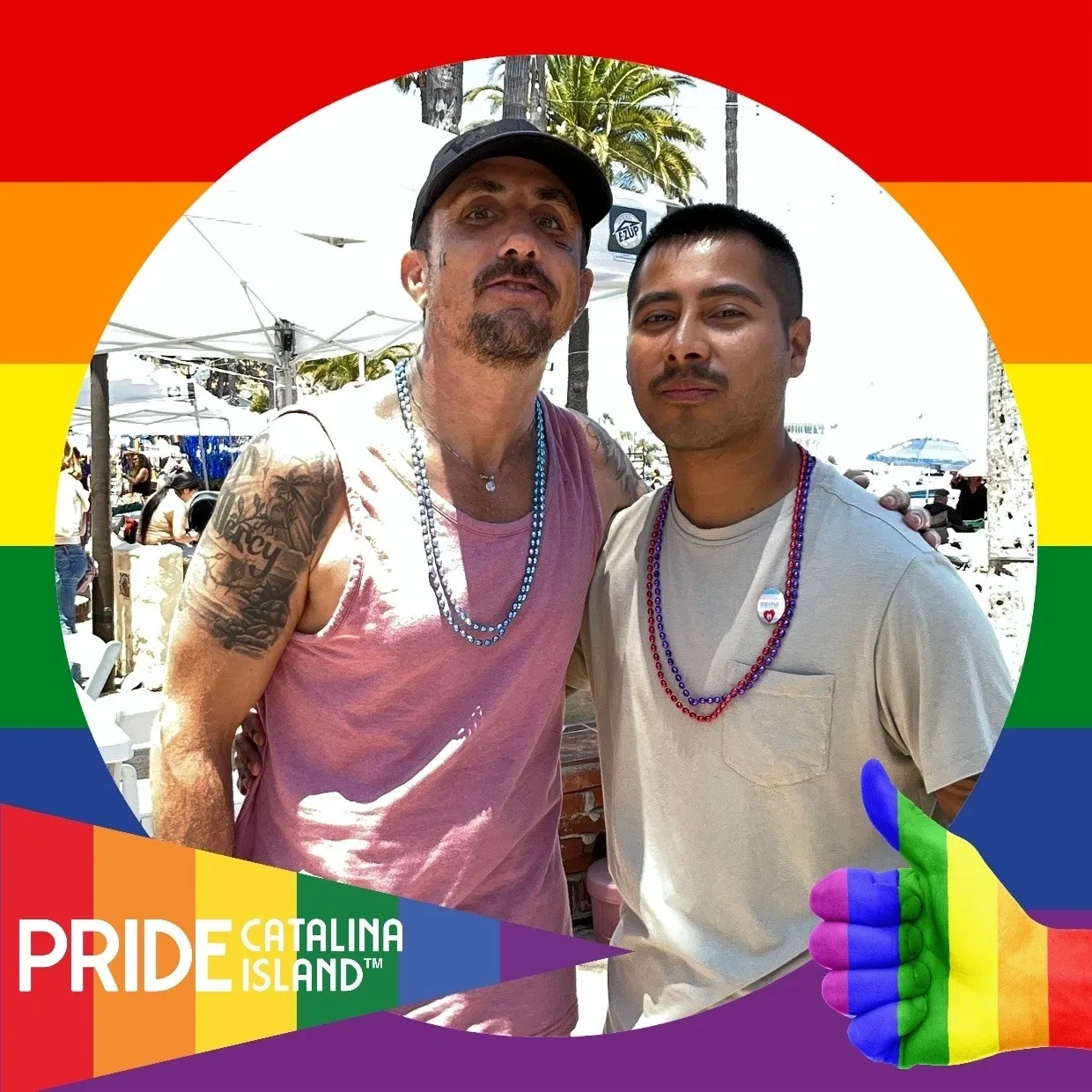 Two men pose for a picture in front of the rainbow flag.