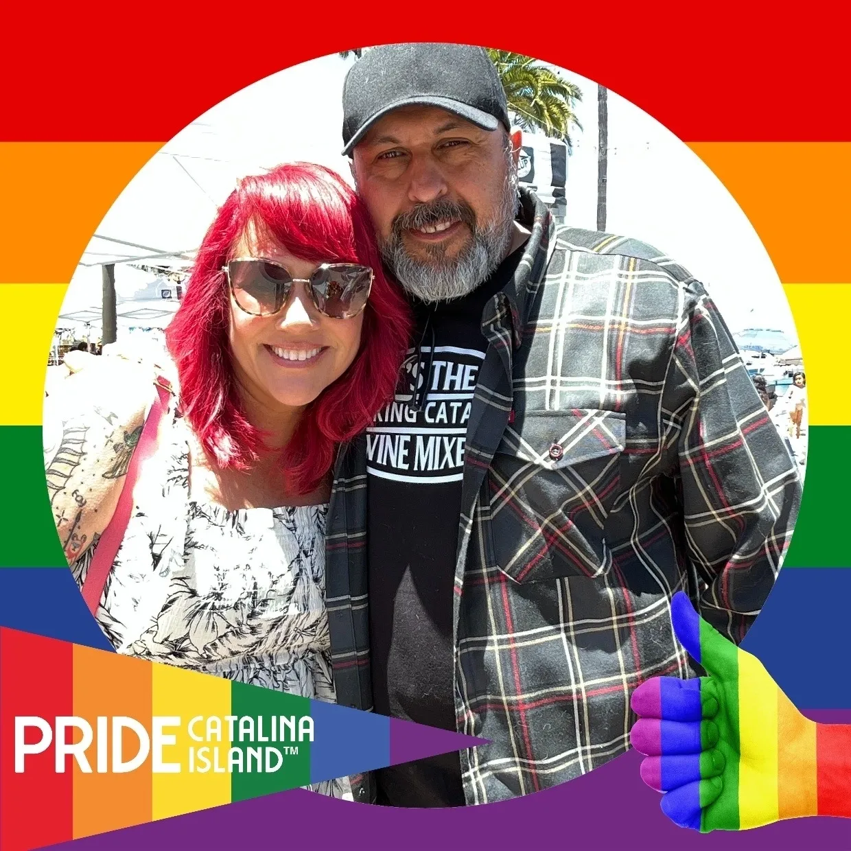 A man and woman pose for the camera in front of rainbow flags.