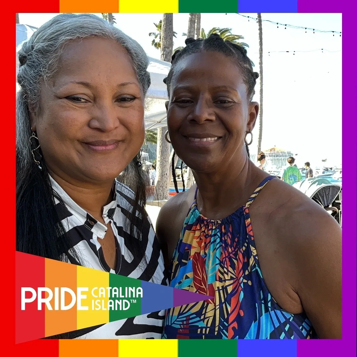 Two women standing next to each other in front of a rainbow background.