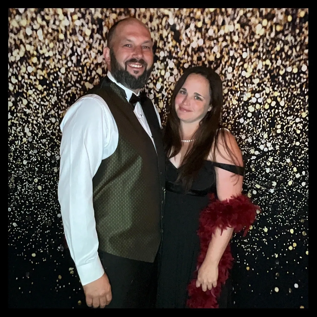 A man and woman pose for the camera in front of a wall covered with gold foil.