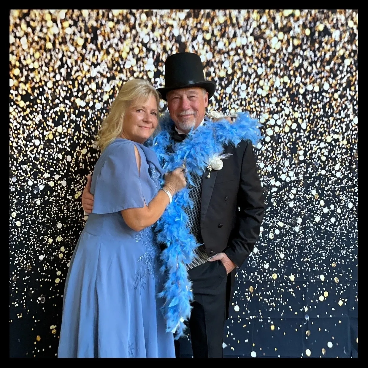 A man and woman posing for a photo in front of a wall covered with confetti.